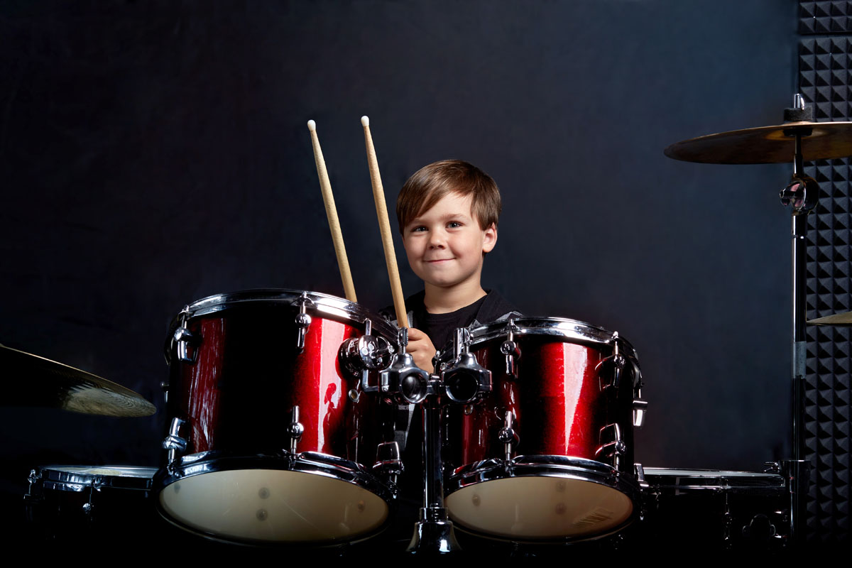 Cheerful smiling child plays the drums. Boys Studios. Dark blue background.