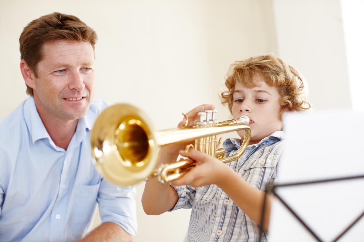 Shot of a cute little boy playing the trumpet while his father watches him proudly.